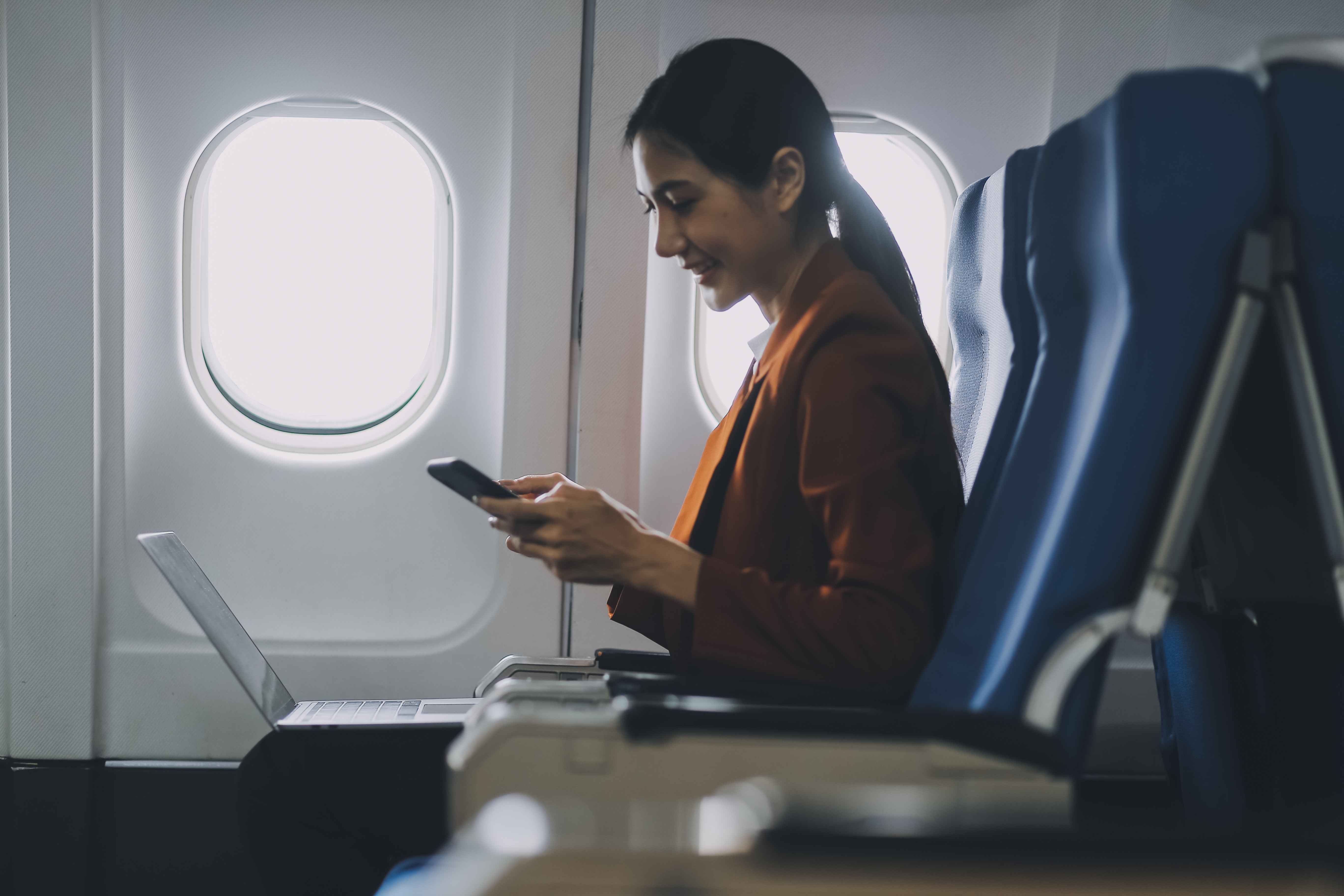 asian-female-tourist-checks-notifications-smartphone-while-seated-airplane-businesswoman-happily-shares-media-from-her-phone-taking-photos-view-from-window-flight_11zon.jpg